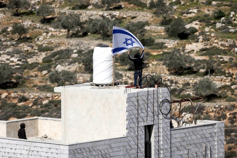 Colonos israelíes izan la bandera de Israel en la casa de Ahed Khatib, dentro de la Zona B cerca de Aqarba, en Cisjordania.