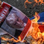 Un manifestante prende fuego a una imagen que muestra la foto policial del presidente estadounidense Donald Trump con la inscripción 'Se Busca'.