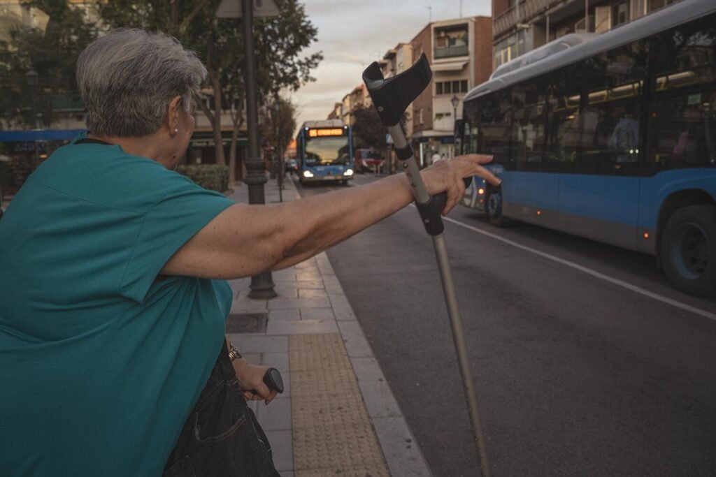Fe tiene una parada de metro a unos pocos minutos de su casa, pero prefiere encaminarse pacientemente hasta la parada de autobús, ya que los pasillos del metro son interminables y las escaleras mecánicas peligrosas de usar con las muletas. Los autobuses, en cambio, son una alternativa más accesible, pero a cambio requieren de aún más paciencia y tiempo, y las marquesinas se transforman en un invernadero en verano y ofrecen una protección escasa contra viento, frío y lluvia en invierno.