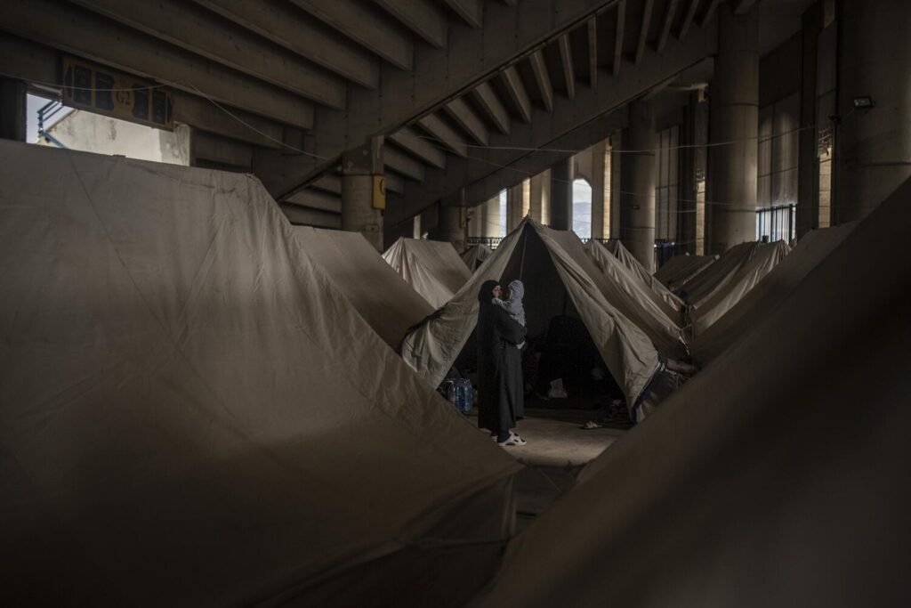 Una mujer sostiene a su bebé frente a su tienda en un campamento improvisado bajo las gradas de un estadio al sur de Beirut.