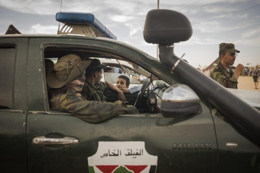 Un niño saluda a dos soldados del ejército saharaui. Tras la ruptura en 2020 del alto el fuego que había regido desde 1991, miles de jóvenes se ofrecieron voluntarios para hacer el servicio militar, recibir entrenamiento y combatir. La actual guerra dista mucho de las batallas que las guerrillas saharauis y las tropas marroquíes libraron en los años 80. Ahora se considera un conflicto de baja intensidad, asimétrico en armamento y tecnología y reducido a lanzamientos puntuales de misiles y artillería saharaui contra posiciones militares marroquíes a lo largo del muro levantado por Marruecos durante miles de kilómetros. Jairo Vargas.
