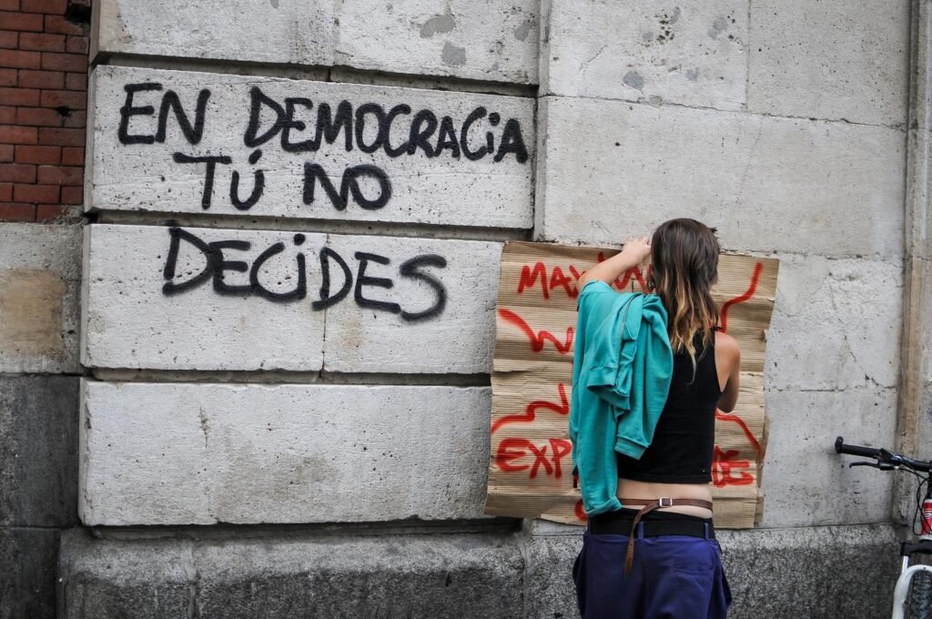 Una joven pega un cartel en el edificio de la Comunidad de Madrid, antigua sede de la DGS, durante la acampada del 15M en la Puerta del Sol en mayo de 2011.