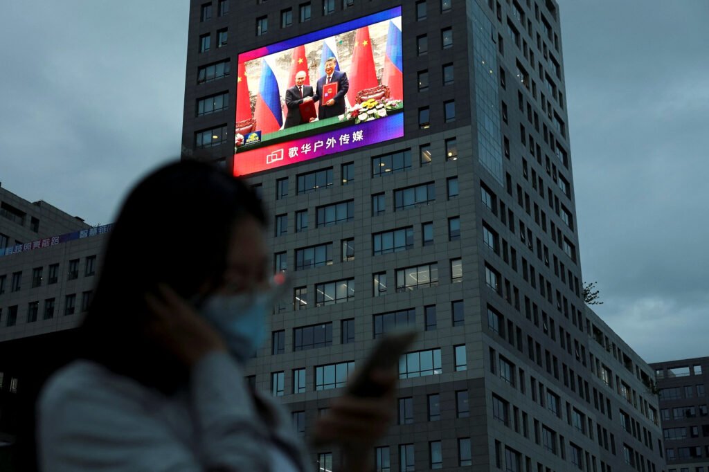 Una mujer cerca de una pantalla gigante que muestra imágenes del encuentro entre el presidente chino Xi Jinping y su homólogo ruso Vladimir Putin.