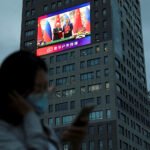 Una mujer cerca de una pantalla gigante que muestra imágenes del encuentro entre el presidente chino Xi Jinping y su homólogo ruso Vladimir Putin.