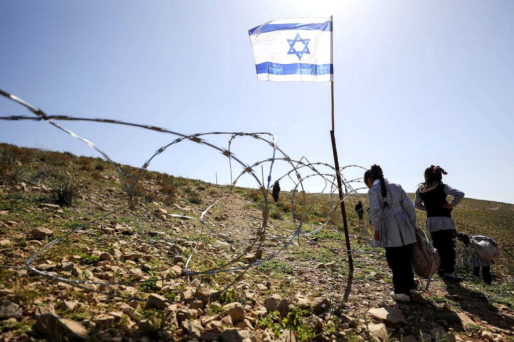 Una valla de alambre de púas con banderas israelíes impide el paso de profesores y alumnos palestinos desde sus casas en la aldea de Umm Al-Khair hasta su escuela, Masafer Yatta, en la Cisjordania ocupada.