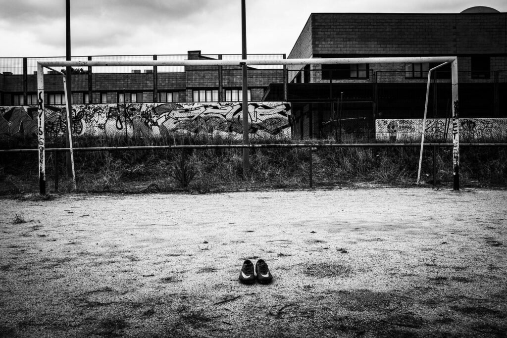 En el centro del punto de penalti descansan las zapatillas que Alex usaba para jugar en el campo de fútbol de su barrio. La imagen, cargada de simbolismo, convierte lo cotidiano en memoria: un espacio que antes estuvo lleno de juego y vida ahora habla del vacío que deja su ausencia, recordando de manera íntima y visible lo que ya no está.
