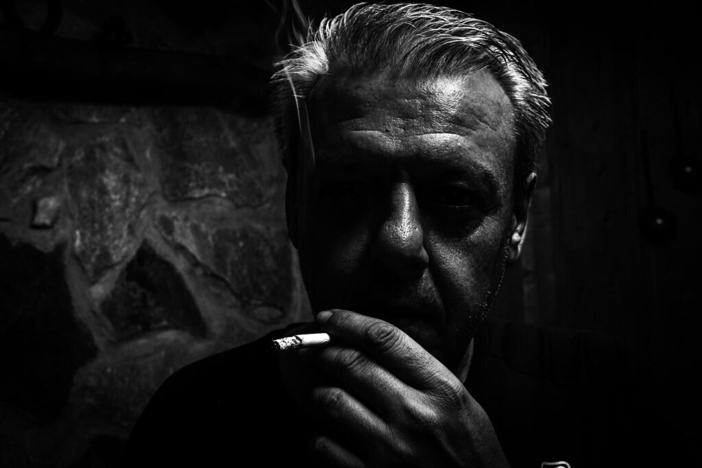 Miguel, padre de Alex, envuelto en un hilo de humo y sombras, transmite la introspección y la carga emocional de la ausencia, convirtiendo un gesto cotidiano en un reflejo silencioso del duelo.