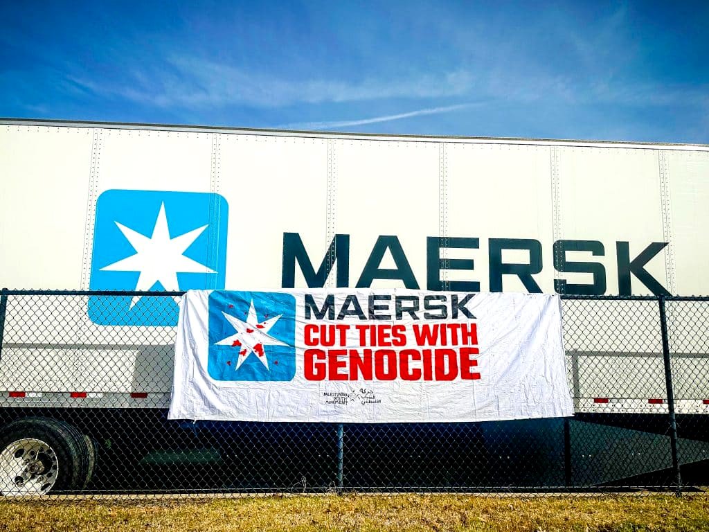 Una pancarta de la campaña 'Fuera la máscara de Maersk' frente a un contenedor de Maersk.