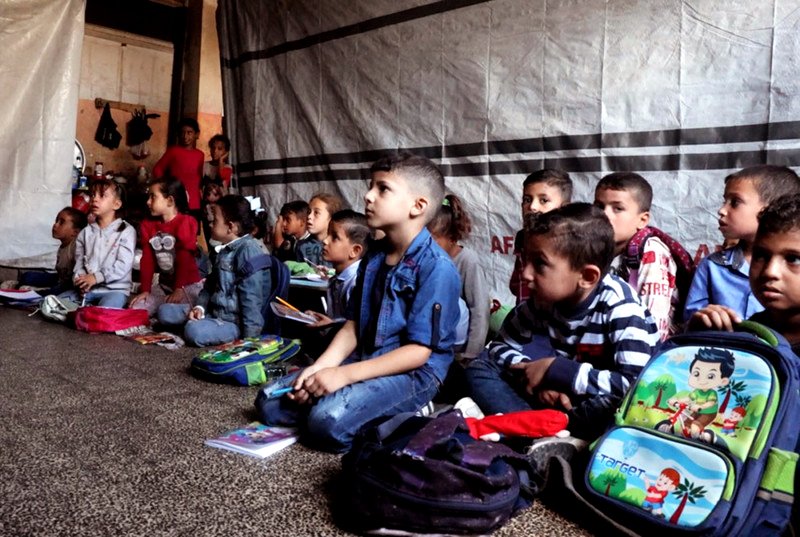 Alumnos sentados en el suelo mientras asisten a clase en una escuela de educación primaria gestionada por la UNRWA.