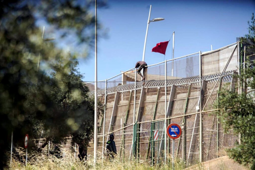 Un hombre tratando de saltar la alambrada en la frontera de Melilla.