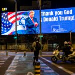 Varias personas pasan junto a un cartel que dice 'Gracias a Dios y a Donald Trump', durante la guerra entre Estados Unidos e Israel contra Irán, en Tel Aviv.