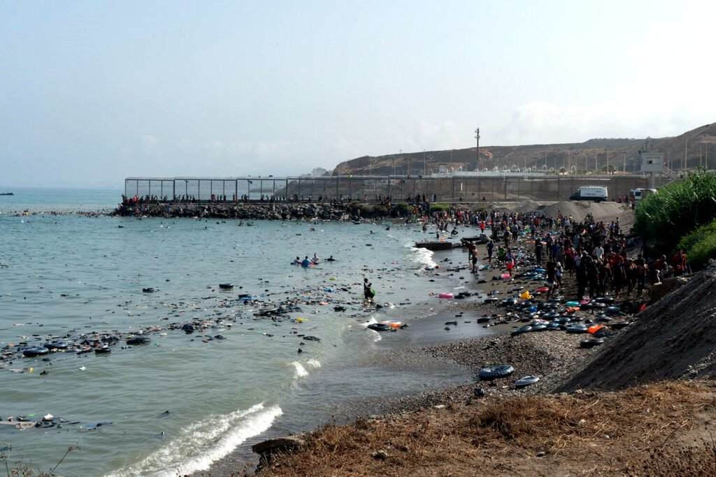 Decenas de personas caminan por la playa de Ceuta tras superar el espigón del Tarajal el pasado 30 de julio.