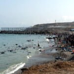 Decenas de personas caminan por la playa de Ceuta tras superar el espigón del Tarajal el pasado 30 de julio.