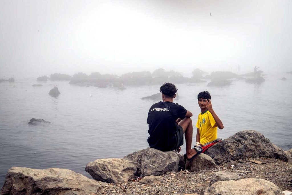 Dos personas en la playa del Trampolín sentadas junto al mar.
