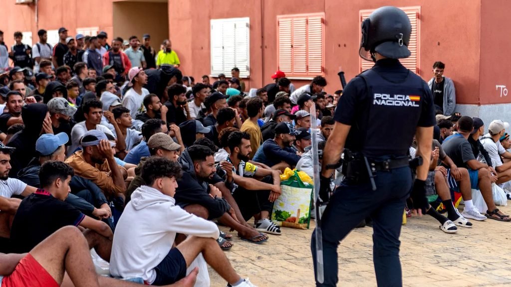Un agente de la policía española monta guardia mientras los migrantes esperan para ser registrados en el distrito de Loma Colmenar de Ceuta el 31 de agosto de 2026.